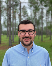 Man with glasses and beard standing in front of a tree